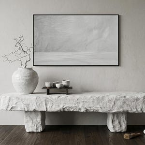 Puede incluir: Un banco de piedra rectangular y largo con una superficie rugosa y texturizada, sostenido por dos patas en bloque. Encima hay un jarr&oacute;n de cer&aacute;mica blanca grande y redondo con una rama desnuda y retorcida, junto a una bandeja oscura peque&ntilde;a.