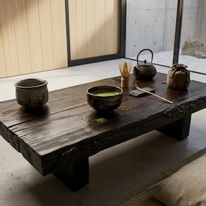 May include: A low, dark-stained wooden coffee table with a live edge, featuring a ceramic bowl filled with green matcha tea, a second empty ceramic bowl, a bamboo whisk, a small dark teapot, a bamboo scoop, and a small fabric pouch.