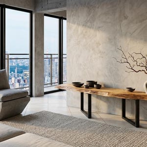 Peut inclure: Un salon moderne avec vue sur la ville. Il comprend un fauteuil gris, une console en bois avec des pieds en métal noir et un vase décoratif avec des branches. La pièce a de grandes fenêtres et une palette de couleurs neutres.