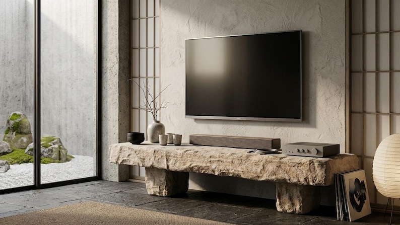 Puede incluir: Un televisor de pantalla plana montado en una pared texturizada sobre un banco de piedra rectangular largo. El banco sostiene una barra de sonido marr&oacute;n oscuro, un receptor electr&oacute;nico gris, un cuenco negro peque&ntilde;o y un jarr&oacute;n gris claro.