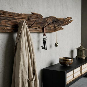 May include: A rustic wooden coat rack with four metal hooks, holding a beige coat, keys, and a pendant. The rack is mounted on a light gray wall, with a dark wooden console table and Japanese-style decor in the background.