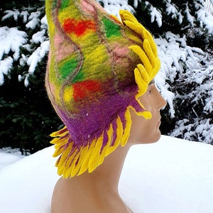 May include: A colorful felted hat with a purple base, yellow fringe, and a green, red, and pink pattern. The hat is on a mannequin head.