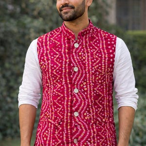 May include: A sleeveless red vest featuring a detailed pattern of white and yellow dots and lines. The vest has a mandarin collar and is fastened with three large, round, white buttons. It is worn over a white long-sleeved shirt.