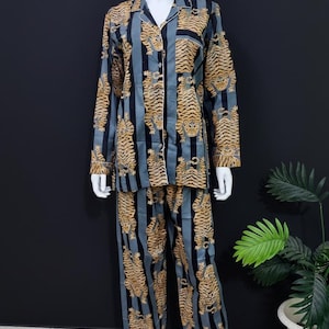 May include: A white ceramic mug with a black handle and the text "But First, Coffee" in a bold, black font. The mug is set against a blurred background, suggesting a cozy setting.