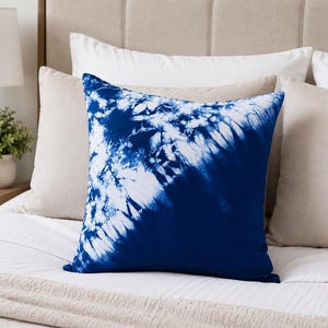 Op de afbeelding: Een vierkant sierkussen met een diepblauw en wit tie-dye patroon. Het ontwerp vertoont een diagonaal verloop, overgaand van een geconcentreerde, ingewikkelde explosie van witte en blauwe patronen in één hoek naar een effen diepblauwe kleur.