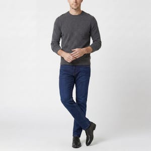 May include: A person wearing a dark gray crew neck sweater and dark blue jeans. The person is also wearing black leather dress shoes. The outfit is simple and classic.