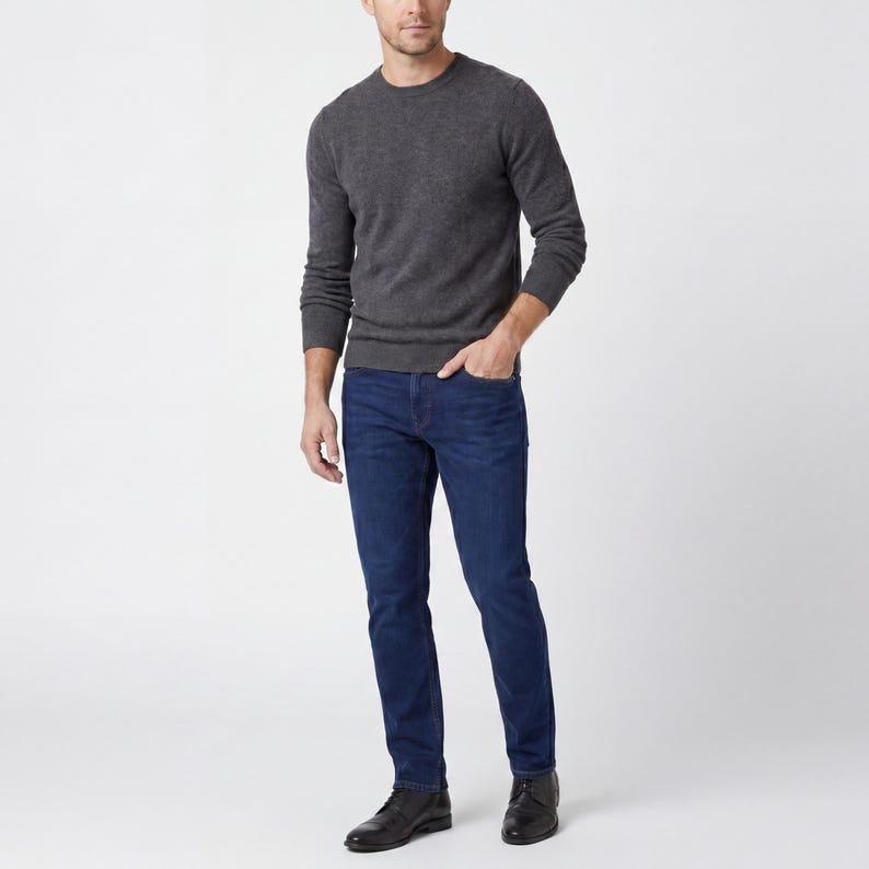 May include: A person wearing a dark gray crew neck sweater and dark blue jeans. The jeans are a classic fit. The person is also wearing black leather boots. The background is plain white.