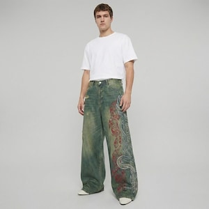May include: A person wearing a white t-shirt and distressed, wide-leg jeans. The jeans are a faded green with a red and white decorative pattern on the side. The jeans have a worn, vintage look.