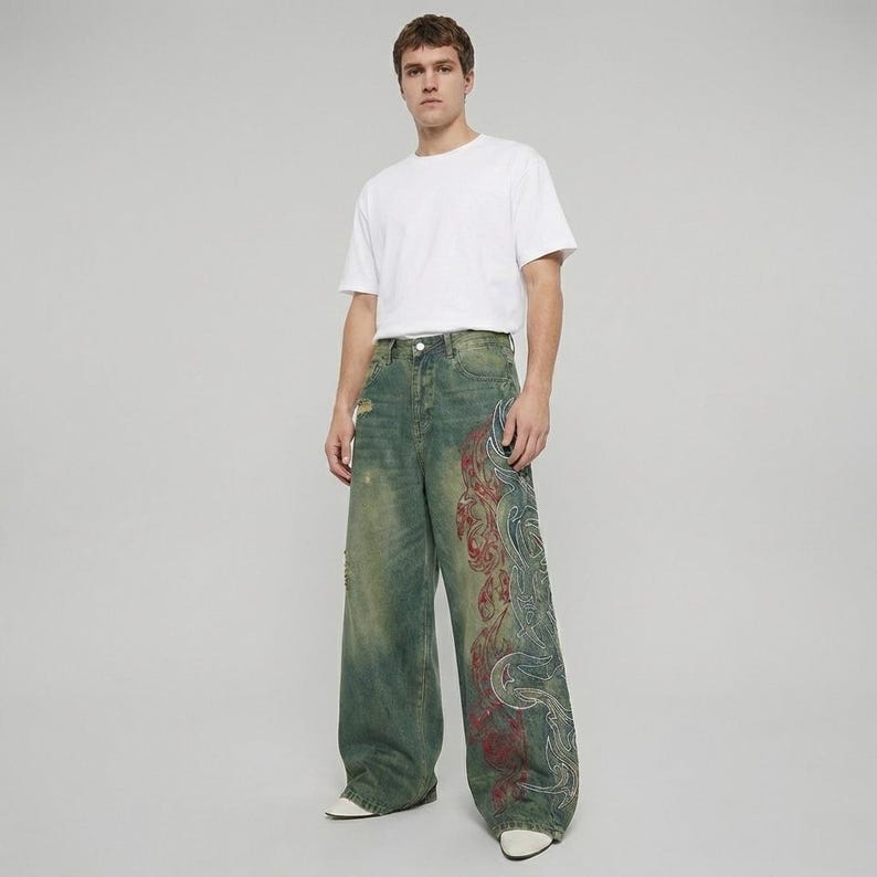 May include: A person wearing a white t-shirt and distressed, wide-leg jeans. The jeans are a faded green with a red and white decorative pattern on the side. The jeans have a worn, vintage look.