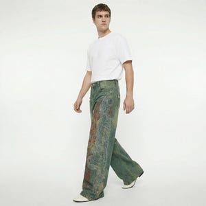 May include: A person wearing a white t-shirt and wide-leg jeans. The jeans are a faded blue-green color with a large, ornate design in red and white on the front of the legs. The person is walking on a white background.