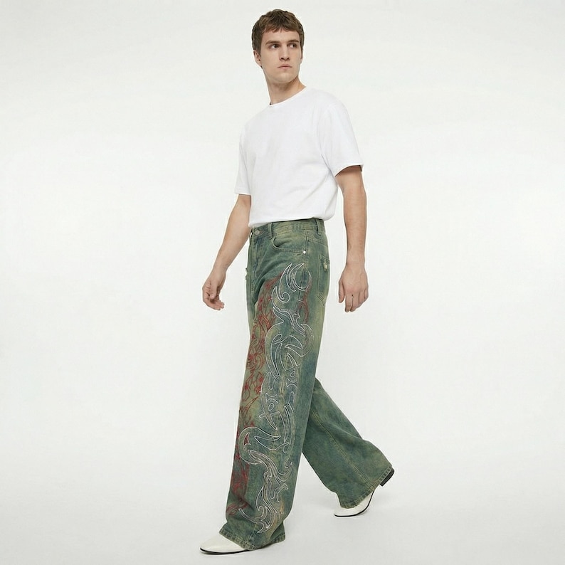 May include: A person wearing a white t-shirt and wide-leg jeans. The jeans are a faded blue-green color with a large, ornate design in red and white on the front of the legs. The person is walking on a white background.