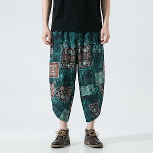 May include: Cropped, loose-fit trousers with a distinctive patchwork pattern. The teal and green background is adorned with red and brown patterned squares. The elasticated waistband and relaxed fit provide comfort. The trousers are worn with brown leather boots.