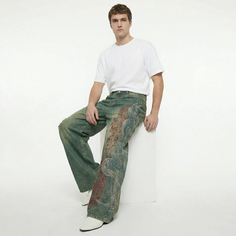 May include: Distressed denim jeans with a faded green wash and a decorative design in red, white, and blue. The jeans have a relaxed fit and are worn with a white t-shirt and white shoes. The jeans feature a unique, artistic pattern.