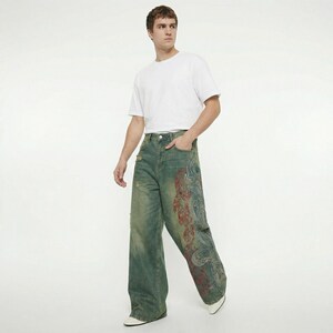 May include: Wide-leg, distressed denim jeans with a faded green wash and a large, ornate red and blue design on the right leg. The jeans have a classic five-pocket design and a button and zipper closure.