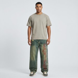 May include: A person wearing a short-sleeved, olive-green t-shirt and distressed, wide-leg jeans. The jeans are a faded blue-green with a red and white decorative design on the side. The person is wearing sneakers.