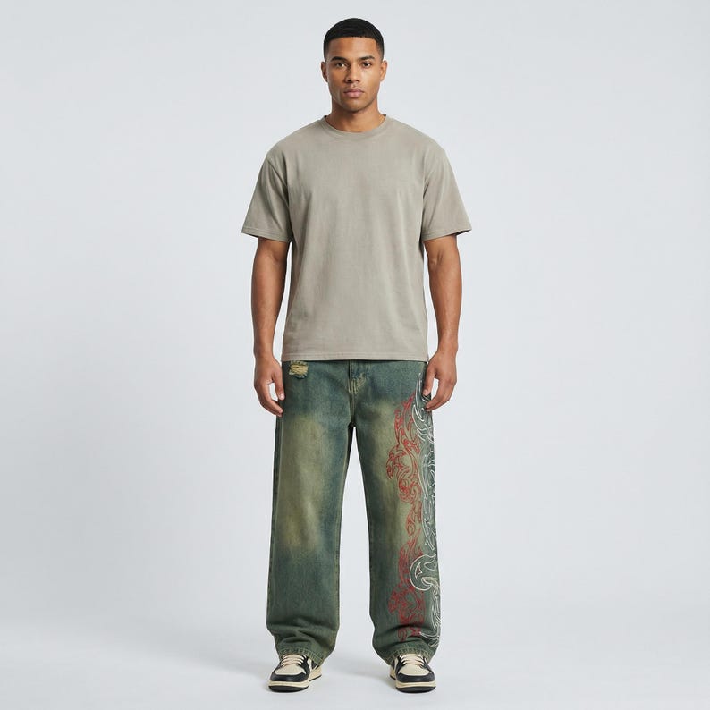 May include: A person wearing a short-sleeved, olive-green t-shirt and distressed, wide-leg jeans. The jeans are a faded blue-green with a red and white decorative design on the side. The person is wearing sneakers.