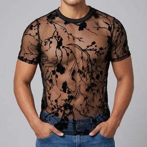 Op de afbeelding: Zwart doorschijnend T-shirt met korte mouwen en een bloemen takken patroon. Het shirt heeft een ronde hals en wordt gecombineerd met een blauwe jeans. Het bloemenontwerp is donkerder zwart.