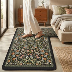 May include: A black floral patterned rug with a rectangular shape and a matching runner. The rug features a detailed design with orange, green, and white flowers and foliage. The rug is placed on a light-colored floor.