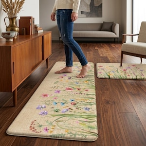May include: Two floral design rugs. The larger rug is rectangular, and the smaller rug is rectangular with rounded corners. Both rugs feature a beige background with a watercolor design of colorful wildflowers and green grass.