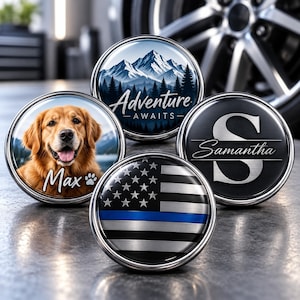 Könnte beinhalten: Vier runde Autoembleme aus Metall mit silbernen Rändern. Eines zeigt einen Golden Retriever mit dem Namen Max und einer Pfote. Ein weiteres zeigt eine Berglandschaft mit dem Text Adventure Awaits. Eines zeigt einen großen Buchstaben S mit dem Namen Samantha. Das letzte zeigt eine schwarz-weiße amerikanische Flagge mit einer dünnen blauen Linie.