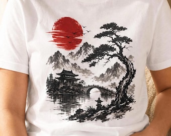 Peut inclure: Un t-shirt blanc à manches courtes orné d'un motif graphique en noir et blanc représentant un paysage avec une pagode, un pont, un grand pin et des montagnes, accentué par un grand soleil rouge circulaire dans le coin supérieur gauche.