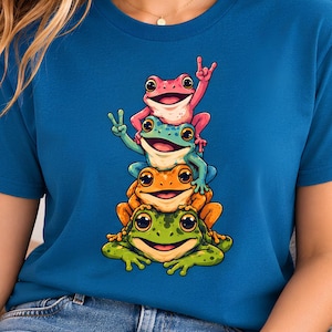 Könnte beinhalten: Ein blaues Kurzarm-T-Shirt mit einem Grafikdruck von vier gestapelten Fröschen. Der oberste Frosch ist rosa, der zweite blau, der dritte orange und der unterste Frosch ist grün. Die Frösche zeigen verschiedene Handgesten, darunter Friedenszeichen.