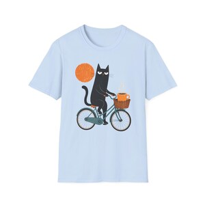 A plain light blue t-shirt displaying a graphic of a black cat riding a bicycle holding coffee.