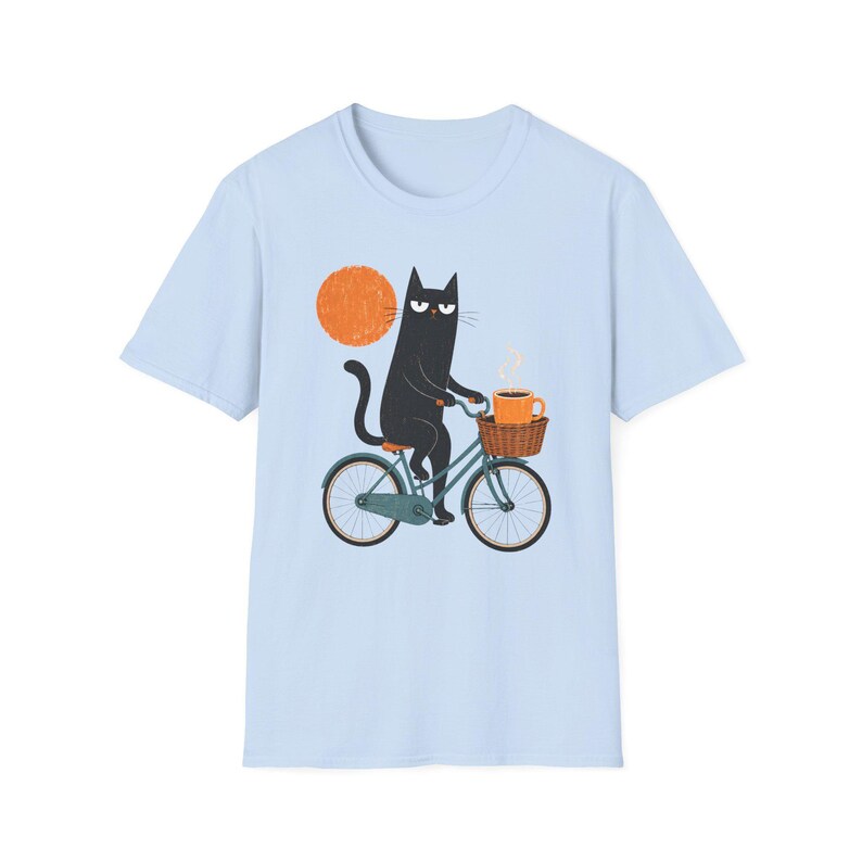 A plain light blue t-shirt displaying a graphic of a black cat riding a bicycle holding coffee.