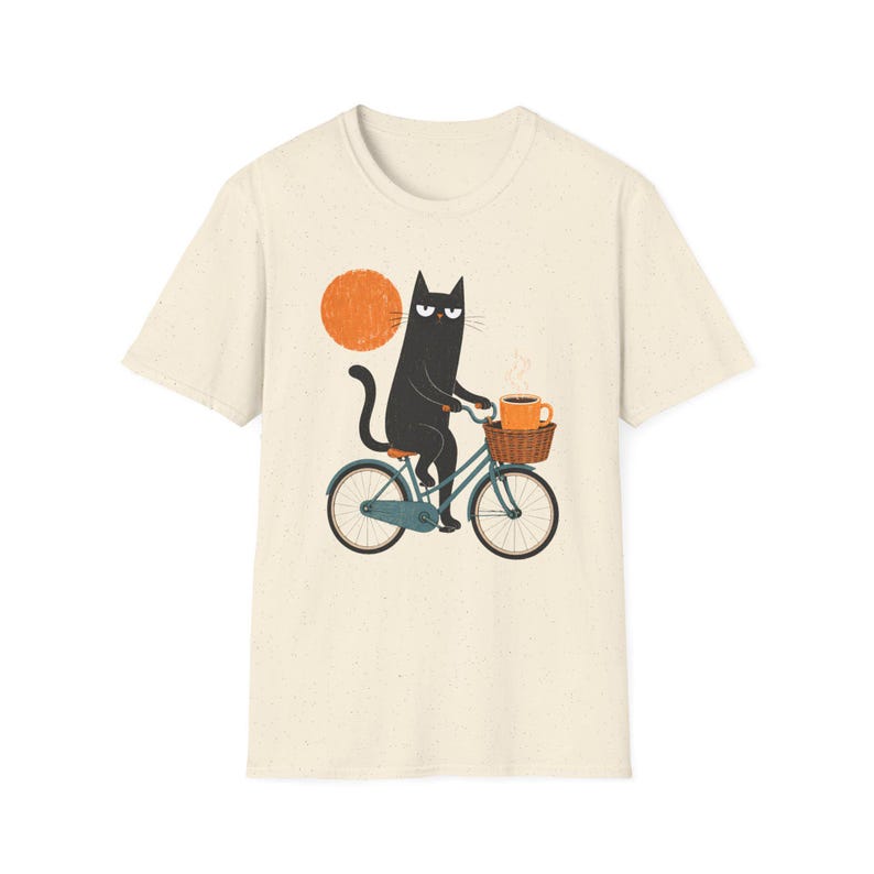 A plain natural-colored t-shirt with an illustration of a black cat riding a blue bicycle with an orange coffee cup.