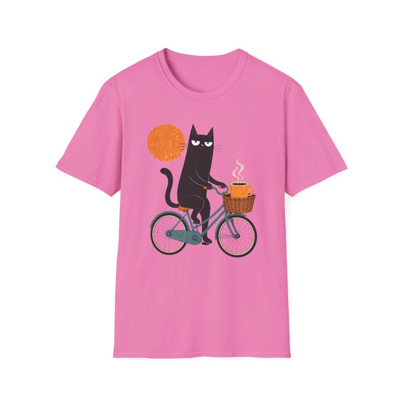 A plain pink t-shirt with a centered graphic of a black cat riding a bicycle with a coffee cup.