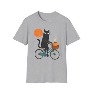 A plain grey t-shirt printed with a graphic of a black cat riding a bicycle next to an orange sun.