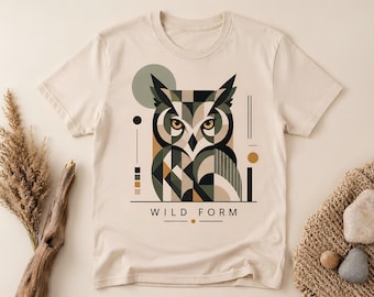 Peut inclure: Un t-shirt à manches courtes de couleur crème arborant un motif géométrique de hibou dans des tons vert olive, noir et beige. Le design comprend des formes abstraites, des lignes et le texte "WILD FORM" imprimé en police sans empattement.