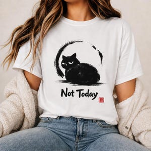May include: A white short-sleeved t-shirt featuring a black ink-style illustration of a grumpy cat sitting inside a circular brushstroke. Below the cat, the text reads "Not Today" in black, accompanied by a small red square stamp.