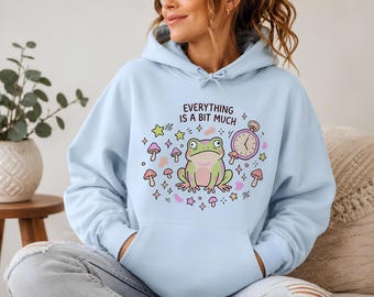 Sweat à capuche unisexe style cottagecore avec motif champignon et horloge, orné d'une grenouille.