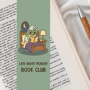 Peut inclure: Marque-page vert avec un dessin animé d'une grenouille en bonnet de nuit lisant au lit. Le marque-page porte l'inscription "LATE NIGHT READER BOOK CLUB" et une petite table avec une lampe et une tasse. Sur un livre.