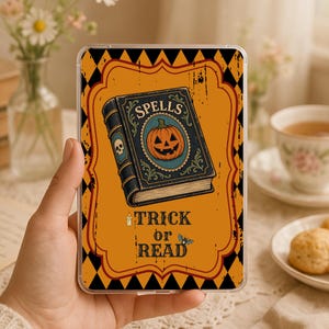 May include: A rectangular clear phone case featuring a graphic of a dark blue spellbook with a jack-o'-lantern on the cover. The background is orange with a black diamond pattern border. Text reads SPELLS, TRICK or READ, with a candle and bat.