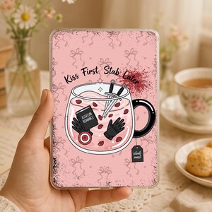 Könnte beinhalten: Eine rechteckige Tablethülle mit rosa Hintergrund und einem sich wiederholenden Schleifenmuster. Die Grafik in der Mitte zeigt eine Tasse mit rosa Flüssigkeit, einen Dolch, ein Buch mit dem Titel Assassin Romance, schwarze Handschuhe und ein Tee-Etikett mit der Aufschrift Silent Roast.