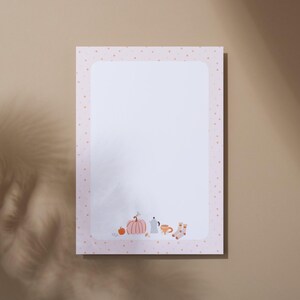 Peut inclure: Une feuille de papier à lettres rectangulaire avec une bordure rose clair à petits pois orange. Le bas de la zone d'écriture blanche présente une petite illustration composée d'une citrouille, d'une cafetière, d'une tasse et de chaussettes.