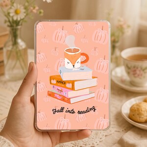 Op de afbeelding: Een rechthoekige tablethoes met een lichtoranje achtergrond en een herhalend patroon van witte pompoenen. In het midden staat een stapel van vier boeken met daarop een mok in de vorm van een vos. De tekst "Fall into reading" is in het zwart.
