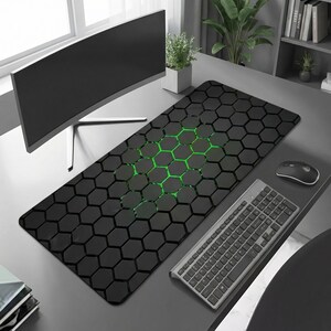 May include: Black rectangular desk mat featuring a honeycomb design with a green gradient. A computer keyboard, mouse, and monitor are on the desk. The mat is designed to protect the desk surface.
