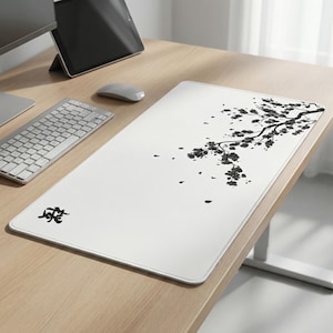 May include: White rectangular desk mat with a black floral branch design. The mat features a minimalist aesthetic, with a Japanese-inspired illustration. The mat is on a light wood desk, with a keyboard, mouse, and tablet visible.