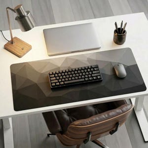 Peut inclure: Un bureau moderne avec un tapis de souris à motifs géométriques gris et noirs. Un clavier noir, une souris argentée et un ordinateur portable fermé sont sur le bureau. Une lampe de bureau en bois et un porte-stylos sont également visibles.