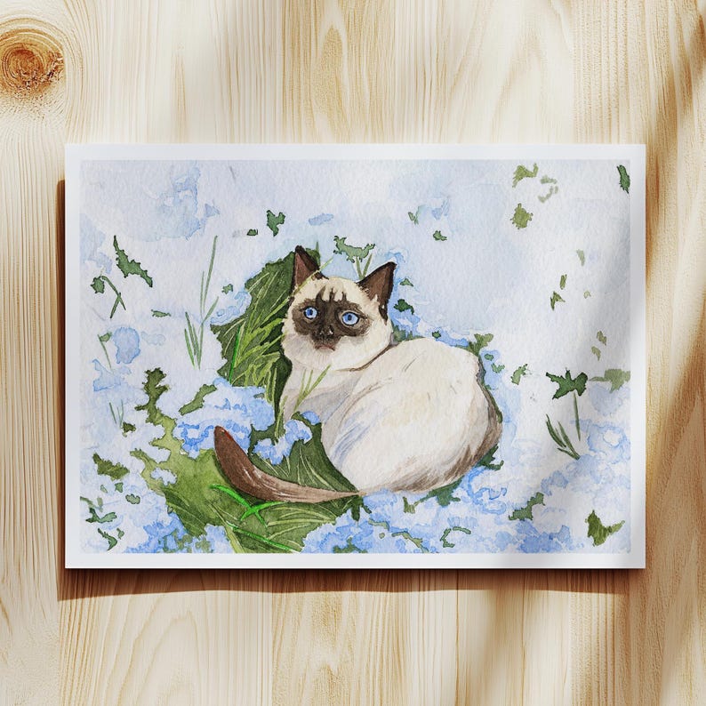 May include: Watercolor painting of a Siamese cat resting among blue flowers and green leaves. The cat has blue eyes, a cream-colored body, and dark brown markings. The artwork is on a white rectangular paper.