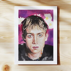 May include: Watercolor portrait of a person with light brown hair and green eyes, wearing a black shirt and a colorful beaded necklace. The background is a mix of purple and pink with white daisy-like flowers. The artwork is on a white rectangular paper.