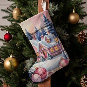 Könnte beinhalten: Weihnachtsstrumpf mit einem Aquarellgemälde einer schneebedeckten Dorflandschaft. Der Strumpf ist rosa und weiß mit einem Winterlandschaftsdesign. Der Weihnachtsbaum ist mit roten und goldenen Kugeln und Tannenzapfen geschmückt.