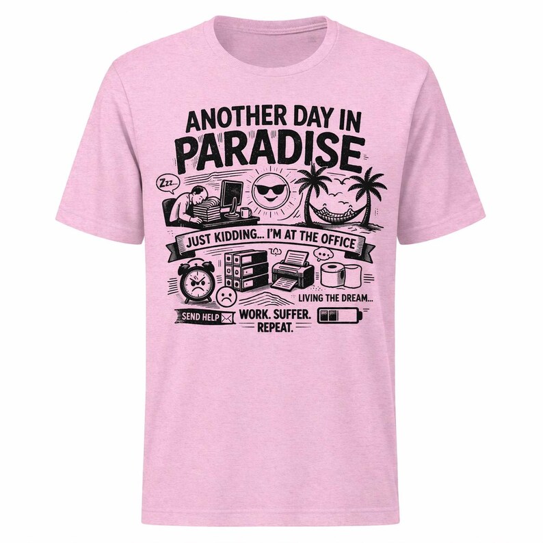 May include: Light pink t-shirt with a black and white graphic. The graphic includes the text "ANOTHER DAY IN PARADISE" and "JUST KIDDING... I'M AT THE OFFICE". Additional illustrations depict office and vacation elements.