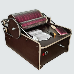 Op de afbeelding: Een houten vezelkaardmachine met twee roterende cilinders met rode borstelharen. De machine heeft een donkerbruin frame met een aan/uit-knop en een netsnoer. Een borstel, schroevendraaier en andere gereedschappen liggen bovenop.
