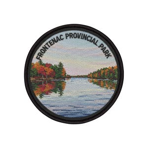 Puede incluir: Parche redondo con una ilustración bordada del Parque Provincial Frontenac. La imagen muestra un lago tranquilo que refleja árboles otoñales coloridos. El texto "FRONTENAC PROVINCIAL PARK" está bordado alrededor del borde.