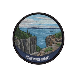 May include: Embroidered patch featuring a scenic landscape with a body of water, cliffs, and trees. The patch is circular with a black border and a blue banner at the bottom that reads "SLEEPING GIANT". The design includes shades of blue, green, and brown.