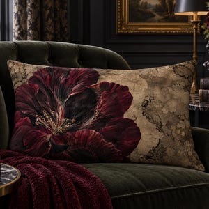 May include: A rectangular throw pillow featuring a large, dark red and black floral print on the left side and a mottled, beige and brown textured pattern on the right side. The pillow is positioned on a dark green, tufted upholstered chair.